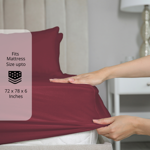 Burgundy fitted bedsheet being stretched over mattress corner with size label showing fits mattress size up to 72 x 78 x 6 inches.