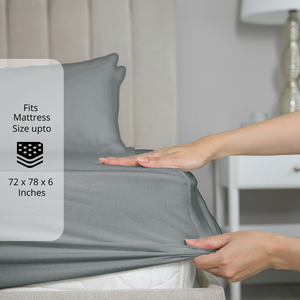 Grey fitted bedsheet being stretched over mattress corner with size label showing fits mattress size up to 72 x 78 x 6 inches.