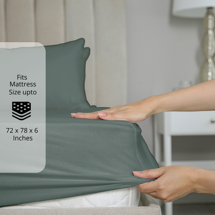  Dark Grey  fitted bedsheet being stretched over mattress corner with size label showing fits mattress size up to 72 x 78 x 6 inches.  