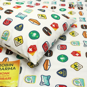 Close-up detail of a soft 210 TC pure cotton kids pillowcase and white bedsheet showing camping and space badge patterns, styled with a book.