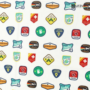 Detailed fabric texture of AURAVE pure cotton kids bedsheet showing colorful printed merit badges like Space Cadet and Shining Star on a white base.