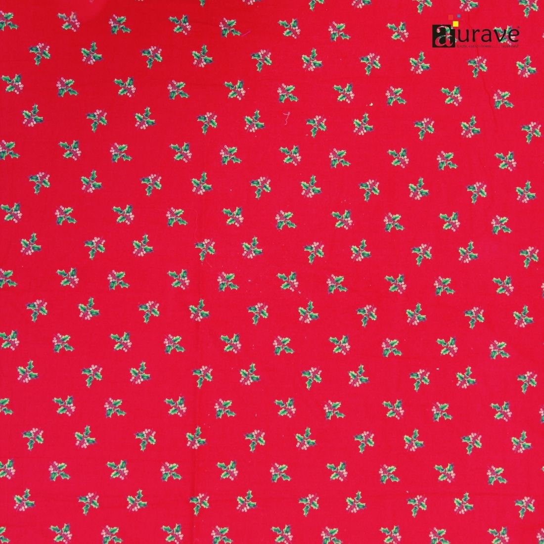 Flatlay texture of AURAVE pure cotton fabric displaying a repeated small green and white holly motif on a solid bright red background.