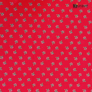 Flatlay texture of AURAVE pure cotton fabric displaying a repeated small green and white holly motif on a solid bright red background.