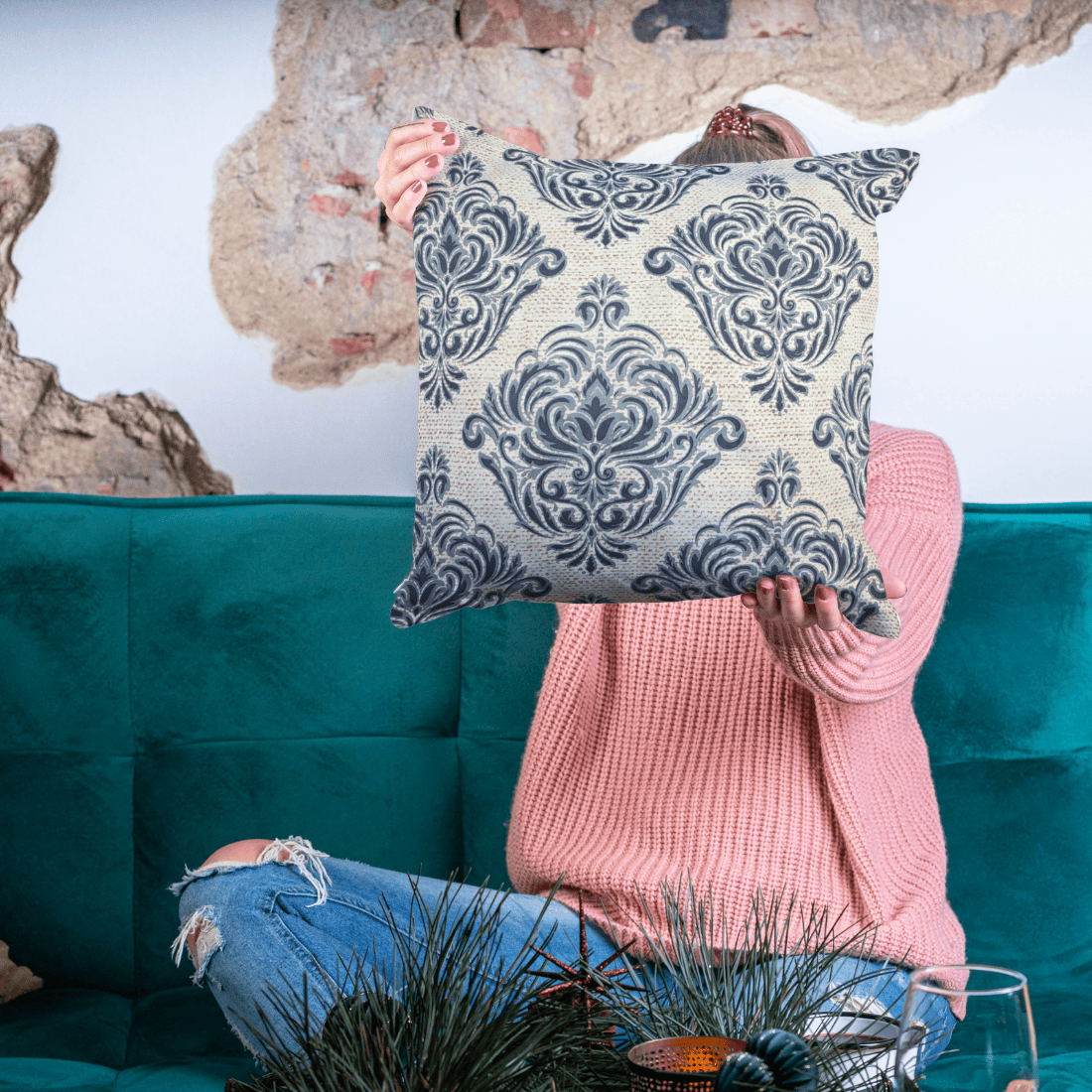 Person holding a decorative pillow with a blue and white pattern in front of a teal couch.