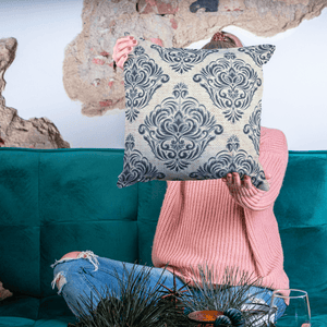Person holding a decorative pillow with a blue and white pattern in front of a teal couch.