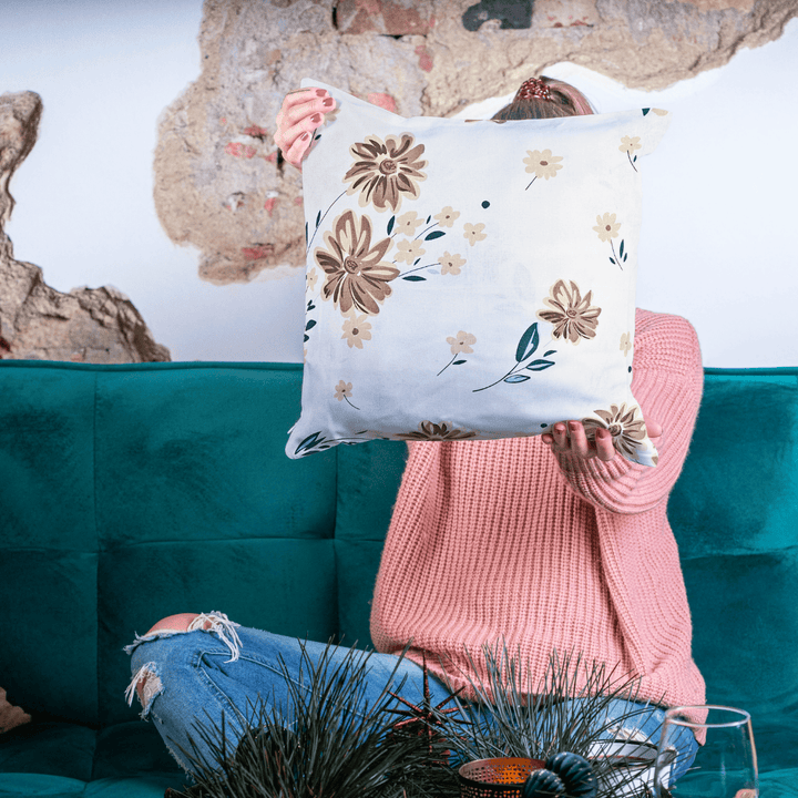 Person holding a decorative pillow with floral patterns in front of a teal couch.