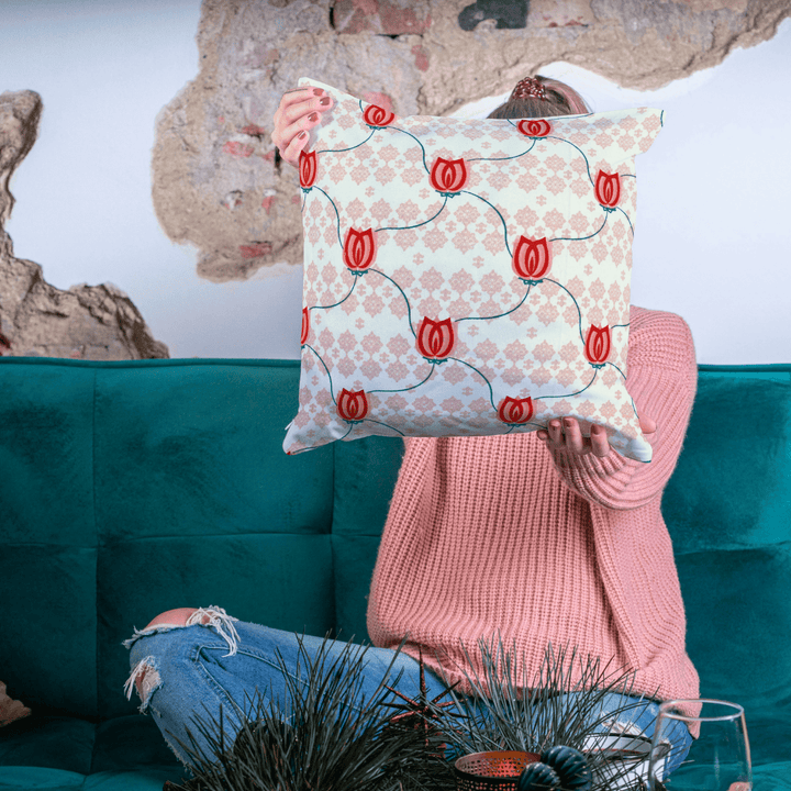 Person holding a decorative pillow with red tulip pattern in front of a teal couch.