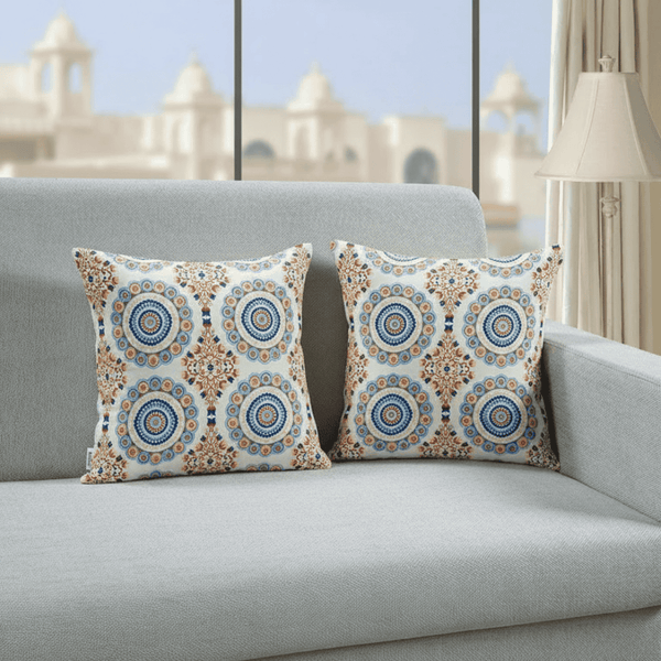 Decorative pillows with circular patterns on a gray sofa in a room with a blurred architectural background.